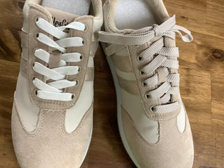 Pair of beige sneakers with white laces on a wooden floor